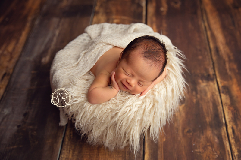 Baby boy smiling while asleep in a basket at his newborn photo shoot. 