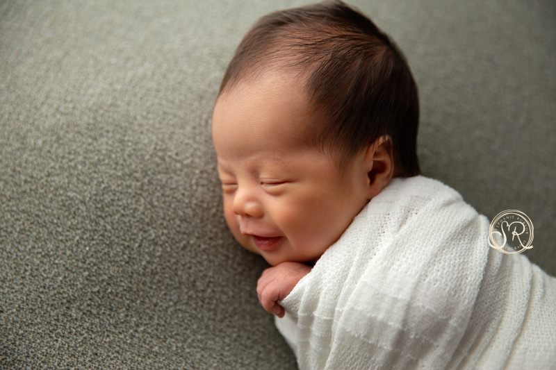Newborn boy smiles as he gets his picture taken.