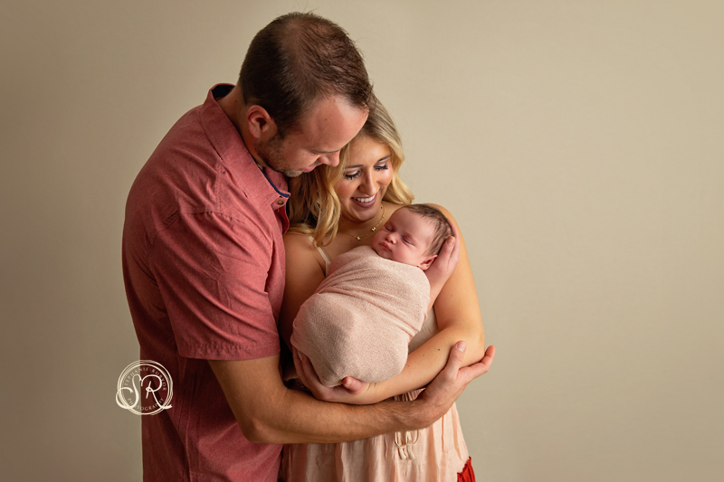 A beautiful new mom and dad holding their newborn daughter in Saginaw photo studio.