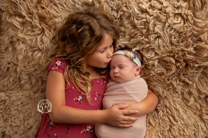 Big sister holding her newborn sister in her arms and giving her a kiss. 
