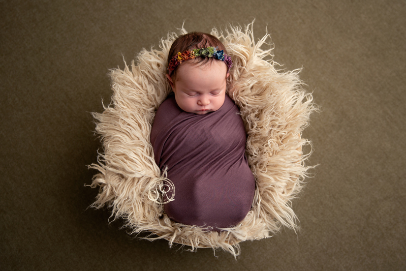 Sleeping newborn girl wrapped in purple laying in a fur lined basket in Fort Worth.