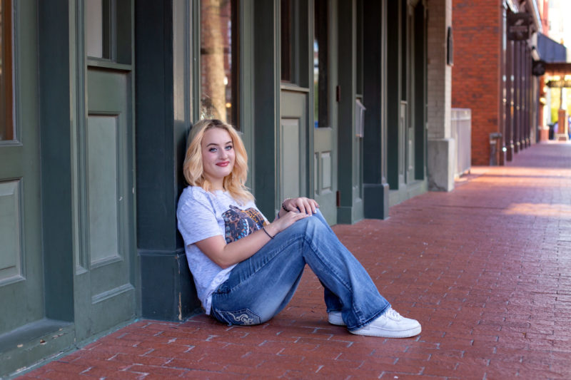 Senior girl sitting on sidewalk in downtown Fort Worth.