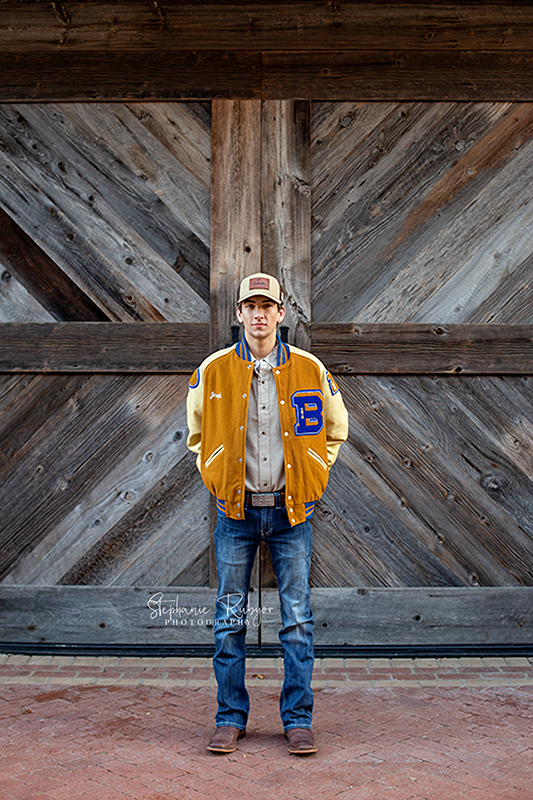 Joseph standing in front of a barn door at the Stockyards for his senior photo session. 