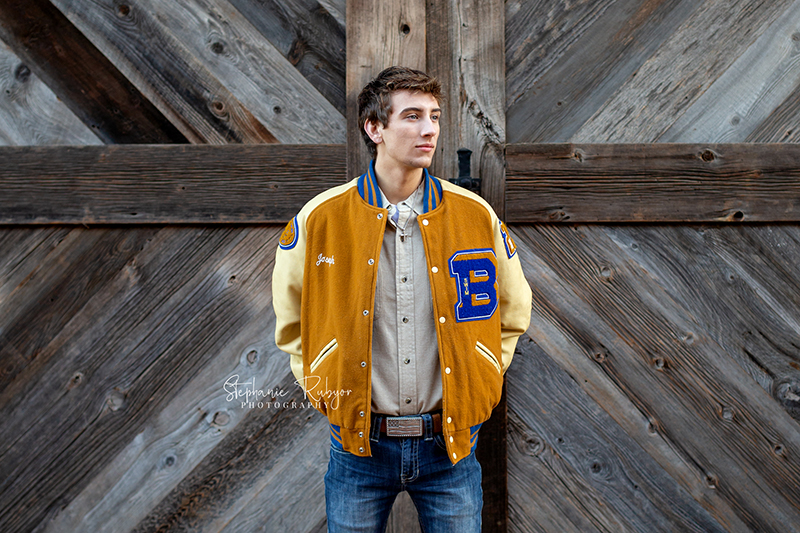 Joseph standing in front of a barn door at the Stockyards for his senior photo session.