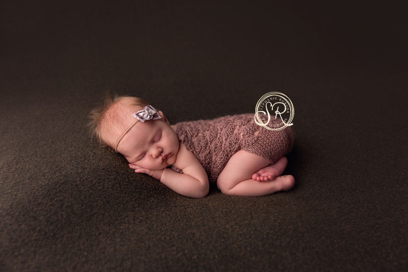 Baby girl in brown romper sleeping at her newborn photo session. 
