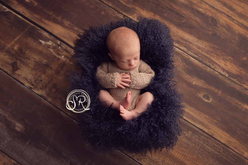 Baby boy sleeping though his newborn session wearing a tan knitted outfit. 