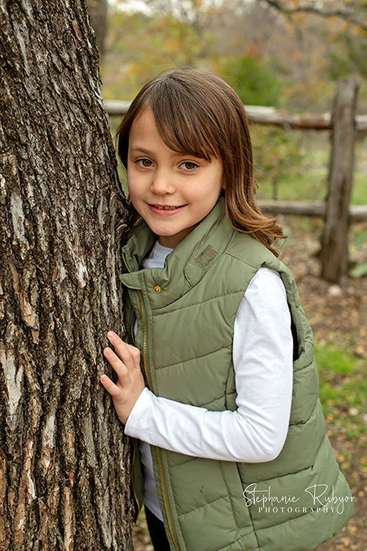 Sweet young girl poses for some family pictures by a tree at a local park. 