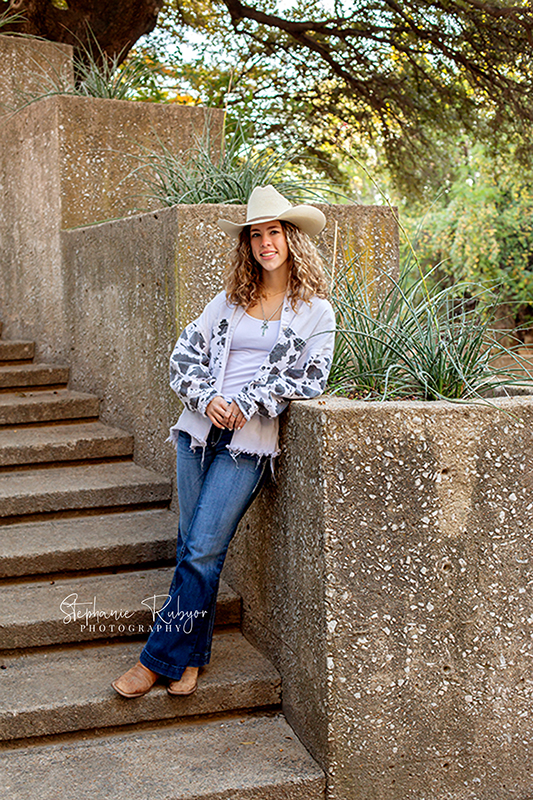 Senior girl in her cowboy poses for her senior pictures on a staircase in Saginaw. 