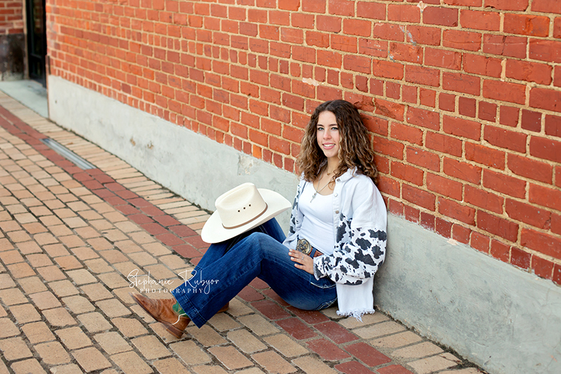 Senior girl poses by a brick wall for her senior photo session captured by Stephanie Rubyor Photography.