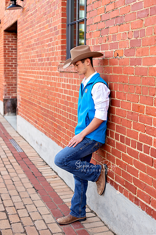 Senior guy poses by a brick wall for his senior photo session captured by Stephanie Rubyor Photography.