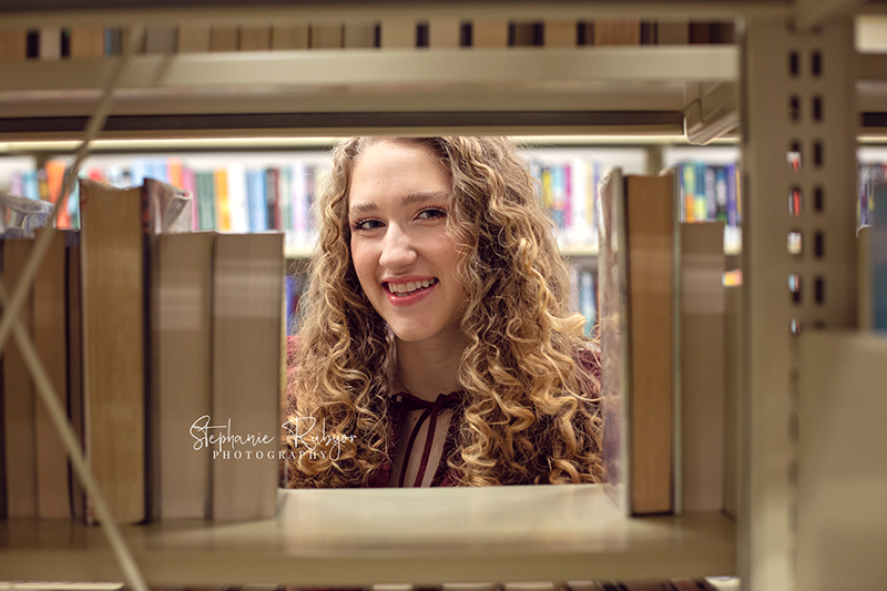 Senior girl peeking through rows of books at her photo session downtown. 