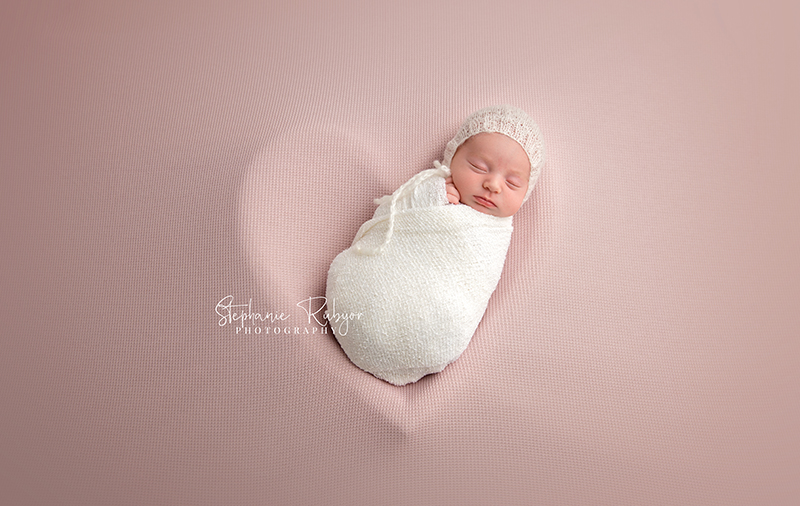 Newborn baby laying in a heart shaped bucket wrapped in white in my Fort Worth photo studio.