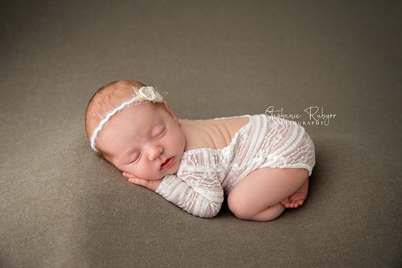 A newborn baby girl iin Fort Worth Texas wearing a lacy white romper asleep on a green blanket.