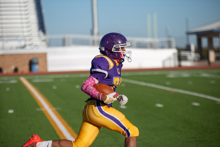 High school football player carrying the ball downfield at local high school football game in Fort Worth, Texas.