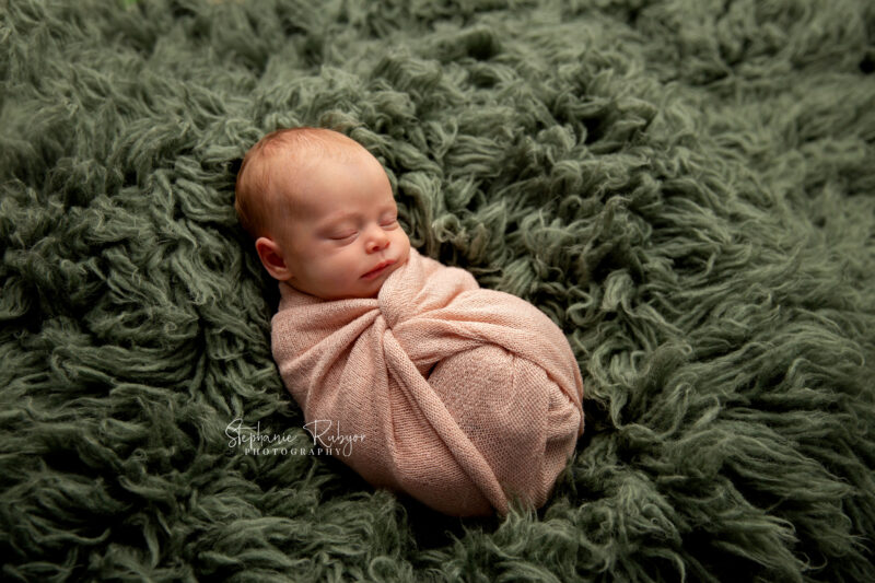 Wrapped newborn baby sleeping on a green fur blanket at a newborn photo session in Fort Worth, Texas.