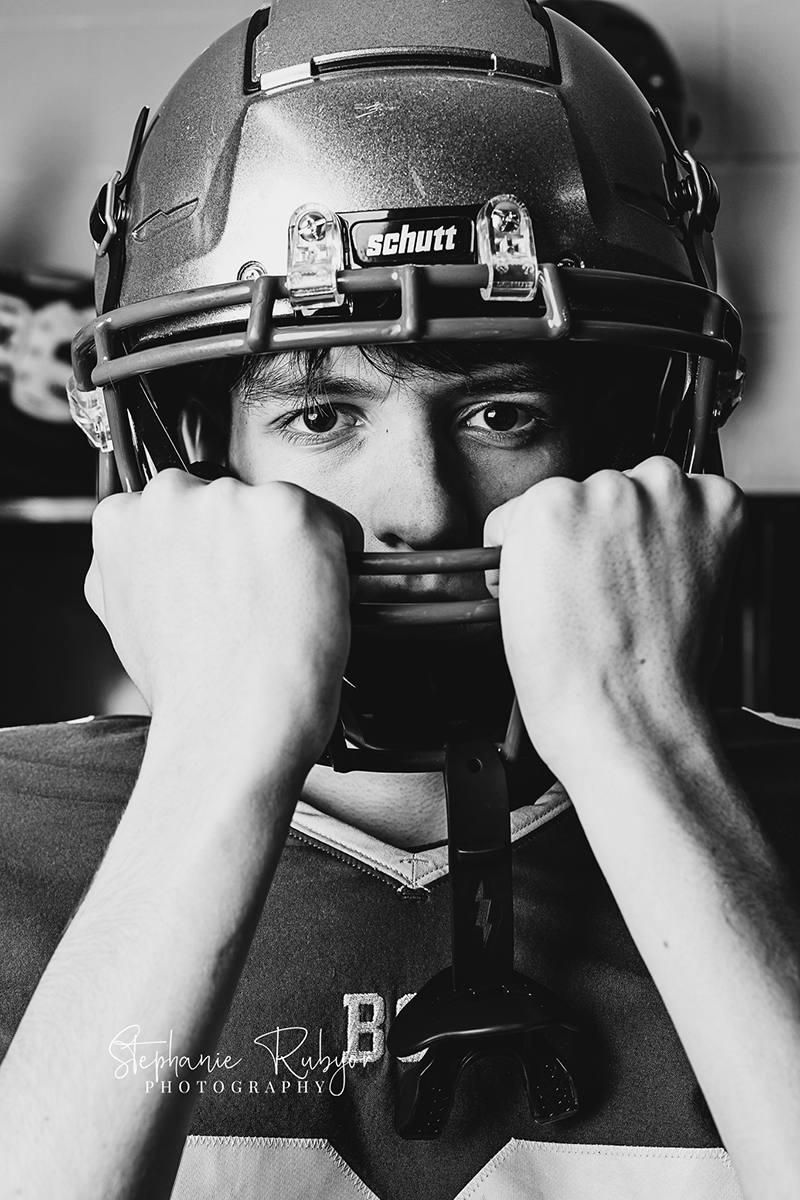 High school senior guy posing in his football uniform for sports portraits at his high school in Fort worth Texas. 