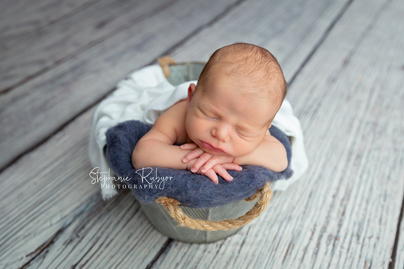 New baby boy posing in a basket wrapped up in white his newborn photo session in Fort Worth.
