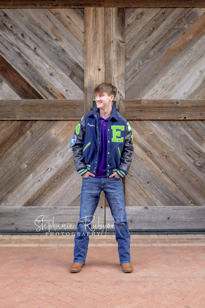 High school senior guy posing for senior portraits in his letter jacket at the Stockyards in Fort Worth, Texas. 