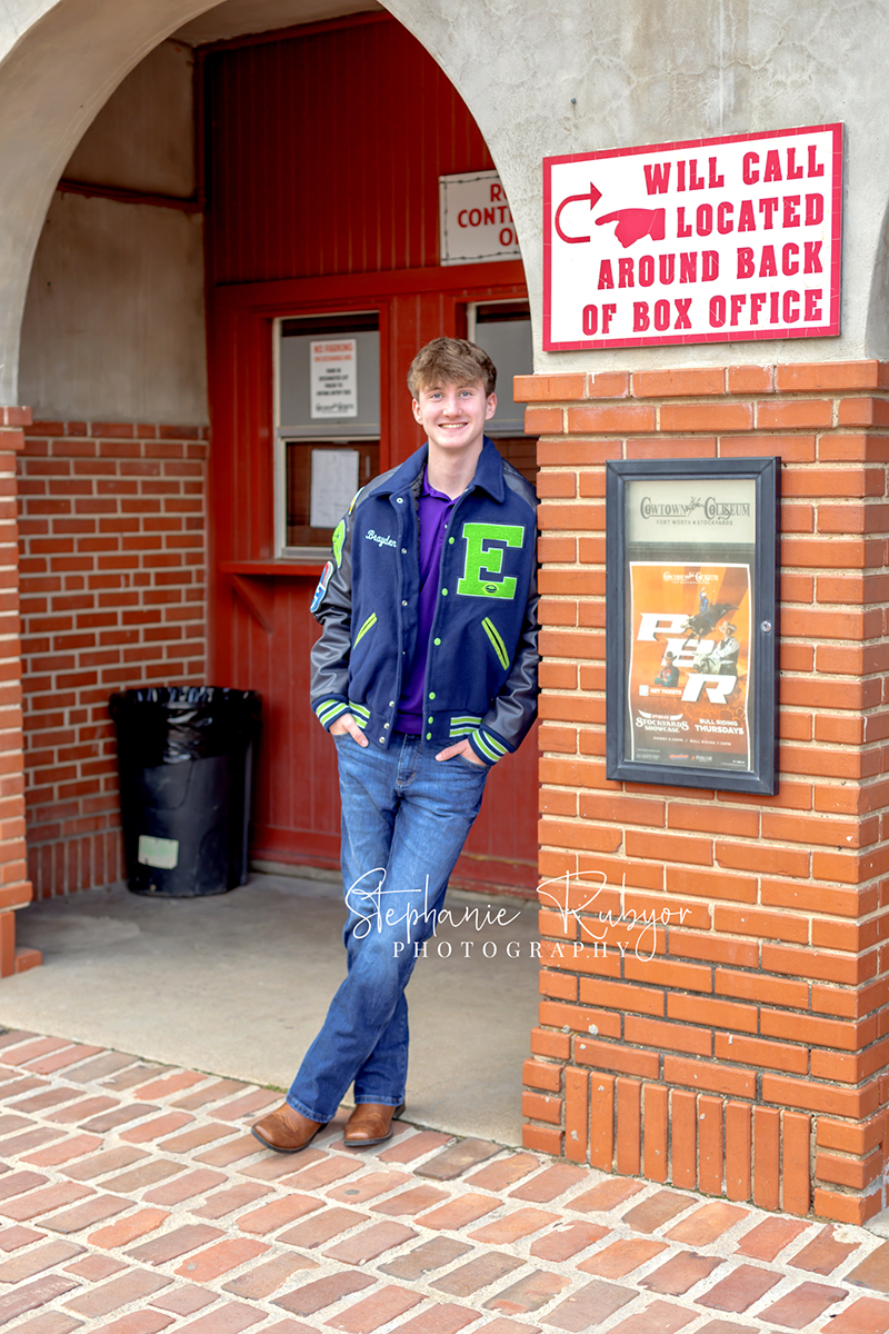 High school senior guy posing for senior portraits in his letter jacket at the Stockyards in Fort Worth, Texas. 