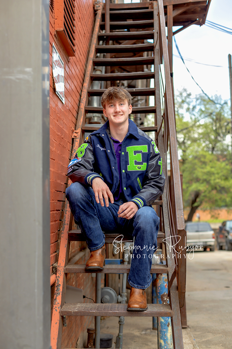 High school senior guy posing for senior portraits in his letter jacket at the Stockyards in Fort Worth, Texas. 