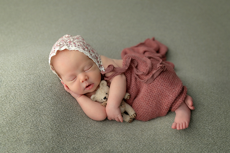 sweet newborn baby posing wrapped in maroon on a green blanket.